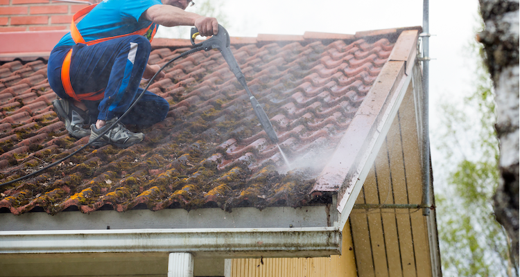 tradesperson with a safety harness cleaning a roof with a pressure washer