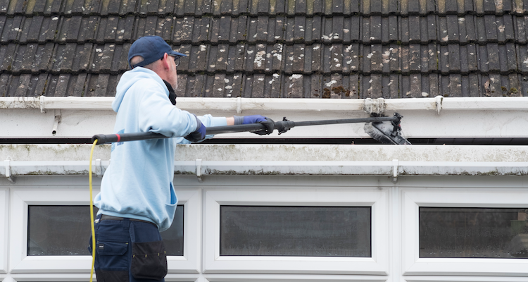 tradesperson with a tool clearing out gutters and cleaning them